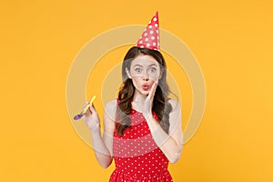 Amazed young brunette woman girl in red summer dress, birthday hat posing isolated on yellow wall background studio