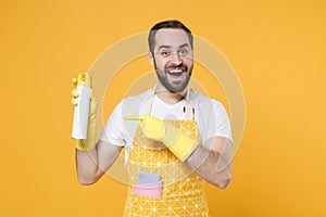 Amazed young man househusband in apron rubber gloves doing housework isolated on yellow background. Housekeeping concept