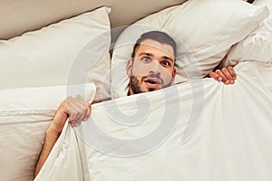 Amazed young man lying in bed at home