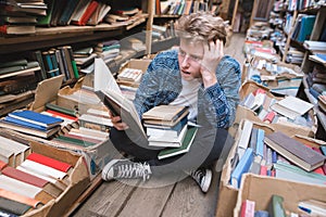 Amazed young man sitting on the floor in a public library and reading a book