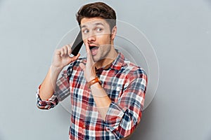 Amazed young man standing and talking on mobile phone
