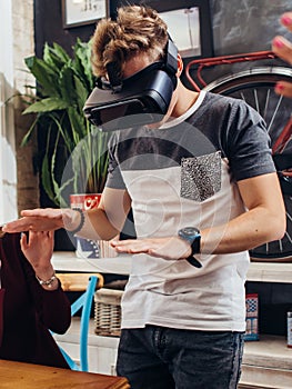 Amazed young man wearing virtual reality goggles playing an interactive game trying to touch something at home