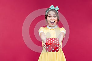 Amazed young woman holding and giving present box to you