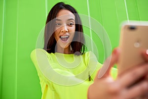 Amazed young woman holds in hands the smart phone to taking self portrait. Teenage girl has surprised expression during