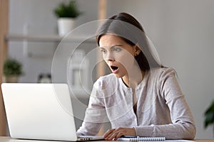 Amazed young woman with opened mouth looking at laptop screen