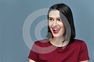 Amazed young woman with red lips posing on blue background. Brunette female model with red lips has joyful expression with