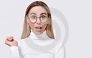 Amazed young woman wears eyewear and casual whote outfit, looking at camera, isolated on white studio background.