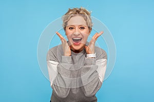 Amazement. Excited woman with short hair in sweatshirt raising hands in surprise and looking startled at camera