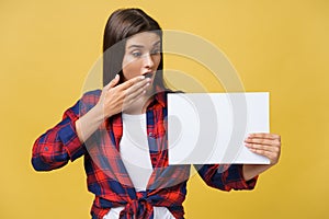Amazement or surprised female with blank white panel, isolated on yellow background.
