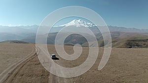 Amazing aerial forward view from highland to snowy peak Elbrus peak. Travel SUV car standing on off road field with