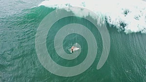 Amazing aerial shot of a professional surfer riding seamless barreling waves. Male surfer paddling and riding perfect