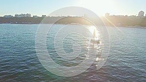 Amazing aerial view of sail yacht sailing near coastline against sunset. Green sea with sun reflections and flares.