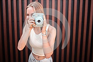 Amazing and attractive young woman is looking straight through camera lenz. She is holding this blue camera in hands
