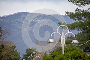 Amazing beautiful view of mountains with inscription `Gelendzhik` from city alley with beautiful lanterns and green trees