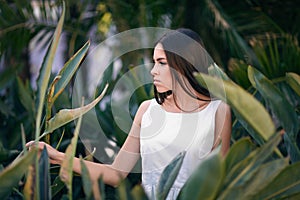 An amazing, beautiful young lady in the tropical forest. The woman in a white dress on fresh and exotic green leaves background.