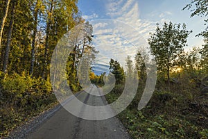 Amazing beauty  sunset on road in autumn forest on blue sky with white clouds.