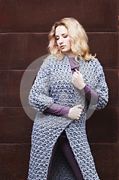 Amazing blonde girl posing in a gray knitted coat on the street on a background of rusty metal wall. fashion. beauty