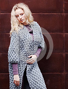 Amazing blonde girl posing in a gray knitted coat on the street on a background of rusty metal wall. Fashion. Beauty.