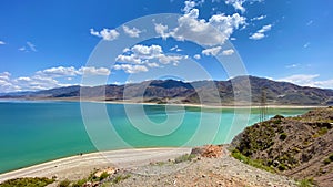 Amazing blue lake in the mountains of Kyrgyzstan. Beautiful summer landscape. Blue sky and white clouds. Journey through