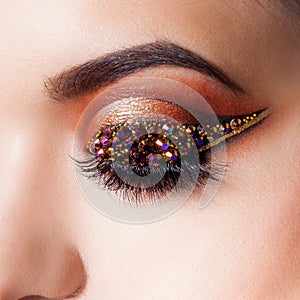 Amazing Bright eye makeup with a arrow with rhinestones. Brown and gold tones, colored eyeshadow photo