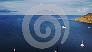 Amazing calm blue sea with floating yachts near cape of island and clear sky above it