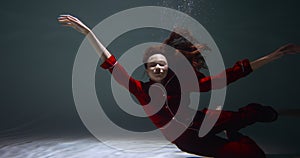 Amazing cinematic portrait of young beautiful woman in red pyjamas slowly sinking under water falling asleep slow motion