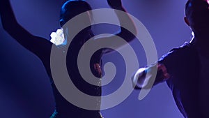 An amazing couple dancing Latin in purple studio light. A young woman in a shiny short dress and a man doing