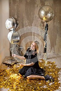 Amazing cute lady celebrating new year birthday party, posing in gold shine background and throwing colorful confetti with silver