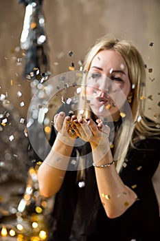 Amazing cute lady celebrating new year birthday party, posing in gold shine background and throwing colorful confetti with silver