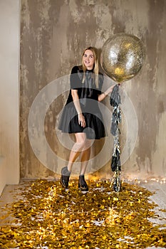 Amazing cute lady celebrating new year birthday party, posing in gold shine background and throwing colorful confetti with silver