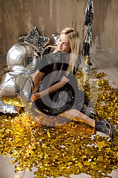 Amazing cute lady celebrating new year birthday party, posing in gold shine background and throwing colorful confetti with silver