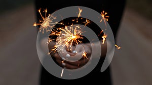 Amazing festive sparklers in the hands of a young woman. Girl celebrates happy birthday. Bright orange sparks with a close up