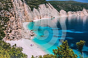 Amazing Fteri beach lagoon, Kefalonia, Greece. Tourists under umbrella chill relax near clear blue emerald turquoise sea