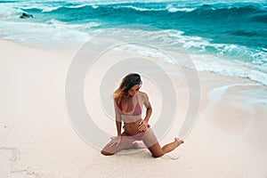 Amazing girl with body is engaged in fitness on the white sand beach. Young women in swimsuit sunbathing on a