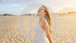 Amazing girl in desert at sunset. Beautiful young fashion woman in white dress breathing enjoying relaxing on the beach