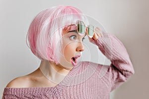 Amazing girl in pink peruke posing with amazement and looking away. Charming female model in colorful wig standing on