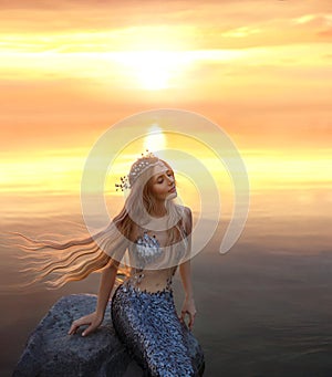 An amazing golden-haired mermaid on the stone in the evening lights of sun