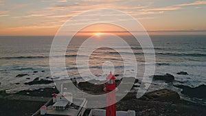 Amazing golden sunset aerial view. Red lighthouse standing on evening seashore.