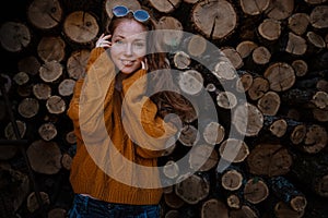 amazing gorgeous redhair girl spins in yellow sweater, jeans and glasses on the background of firewood. Autumn mood