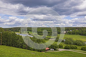 Amazing green summer nature landscape view. Fiew buildings on green fields between green forest trees under blue sky.