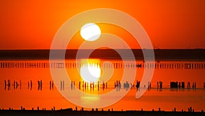 Amazing incredible red sunset with a huge round sun on a salt lake against the backdrop of silhouettes of windmills