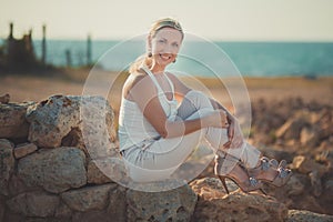 Amazing lady blond woman in light white stylish clothes posing on sea side beach air.Sparkler girl looking to camera on ancie photo