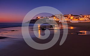 Amazing landscape of the Atlantic ocean coast at dusk. Night view on the village in lights, reflecting on a sandy beach. Portugal. photo