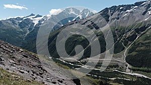 Amazing landscape with giant mountains with green slopes and snowy peaks. Clip. Stony trail along rocks covered by green