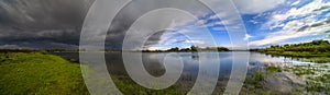 Amazing landscape of nature before thunder storm. Dark clouds cover blue sky at wild river. Incredible weather panorama