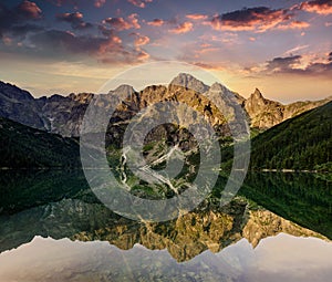 Amazing landscape of Tatra Mountains at sunset. View of high rocks, illuminated peaks and stones, reflected in mountain lake Mors