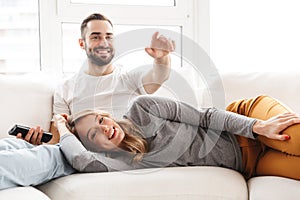 Amazing loving couple sitting indoors at home watch TV holding remote control