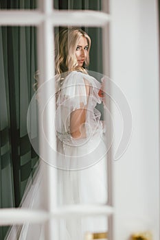 Amazing luxury bride in beautiful white wedding dress looking at us through the window