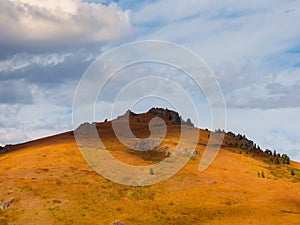 Amazing mountain landscape with cone  rock in golden sunlight under beautiful white clouds. Nature background of rocky mountain