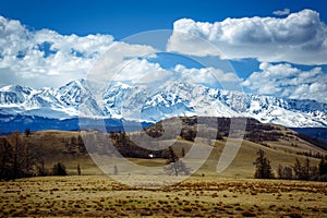 Amazing mountain landscape. Rocky mountains with snowy peaks, hills covered with grass in the Alpine scene on a bright sunny day